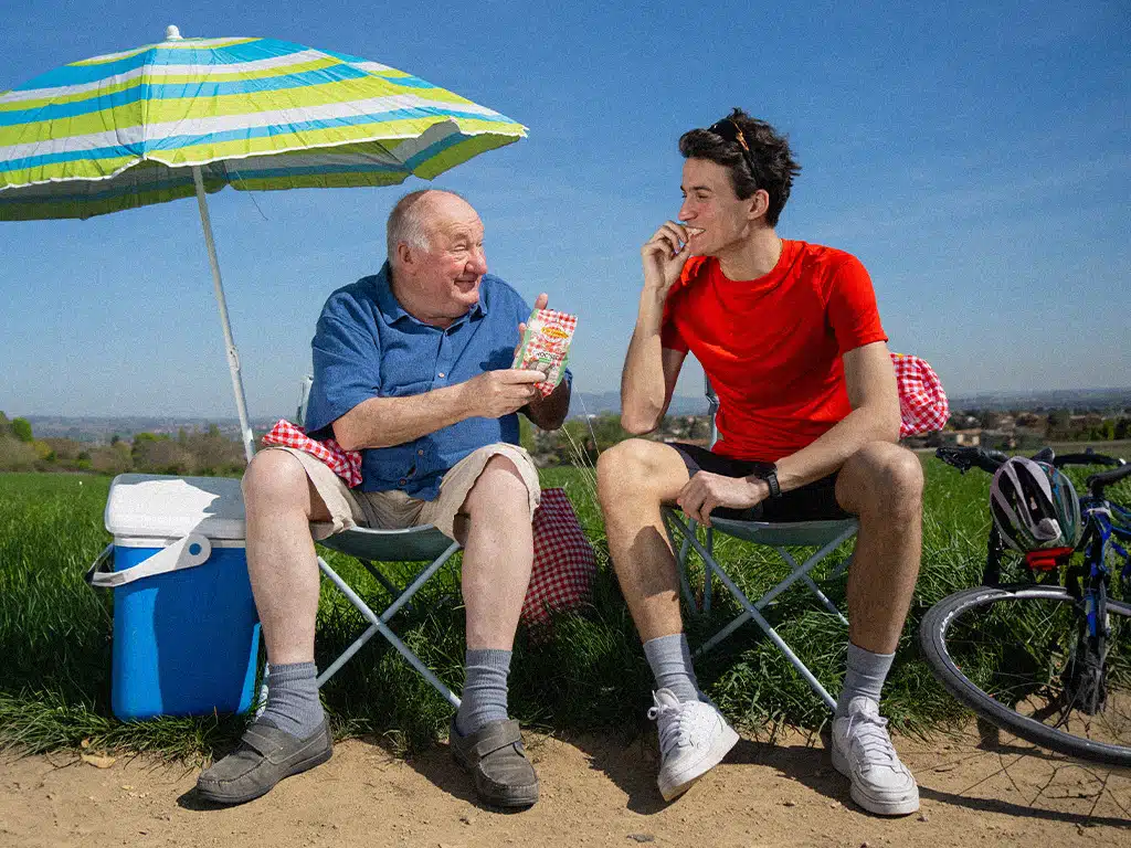 Photo backstage tournage Cochonou - Grand père et petit fils partageantun paquet de Croc'Sec